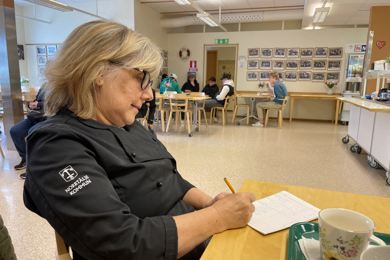Naemi Asklöf sitter i matsalen, elever i bakgrunden.