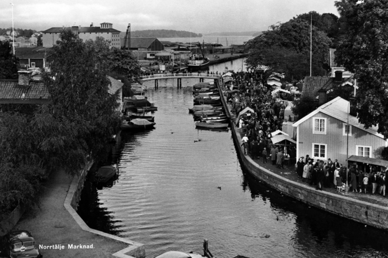 Historiskt svartvit bild med hamninloppet. Bilden är tagen när det är Norrtälje marknad så det är mycket folk i rörelse.