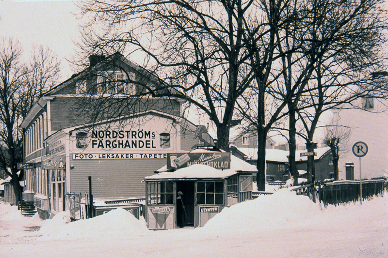 Exteriör bild av Nordströms färghandel. Snö runt byggnaden och på fasaden står texten Nordströms färghandel, foto, leksaker, tapeter.