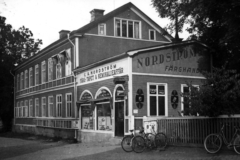 Exteriör bild av Nordströms färghandel. En gul träbyggnad med texten C.A Nordström, färg- tapet och kemikalieaffär som text över dörren.