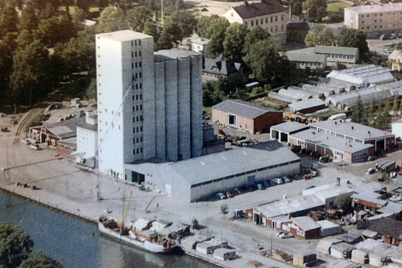 Flygbild över hamnen och silo. Bilden är tagen omkring 1965 och på bilden syns hamnkajen med lastfartyg. Industribyggnader ses runt om silon och längre bak i bilden syns bostadshus.
