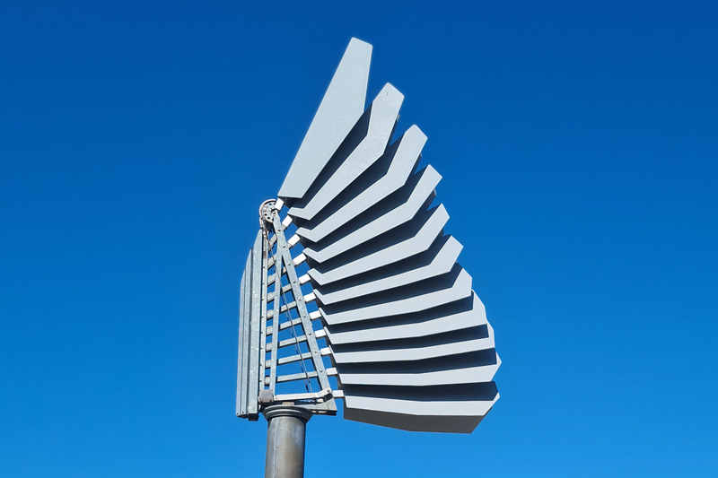 en skulptur av en vinge framför en blå himmel