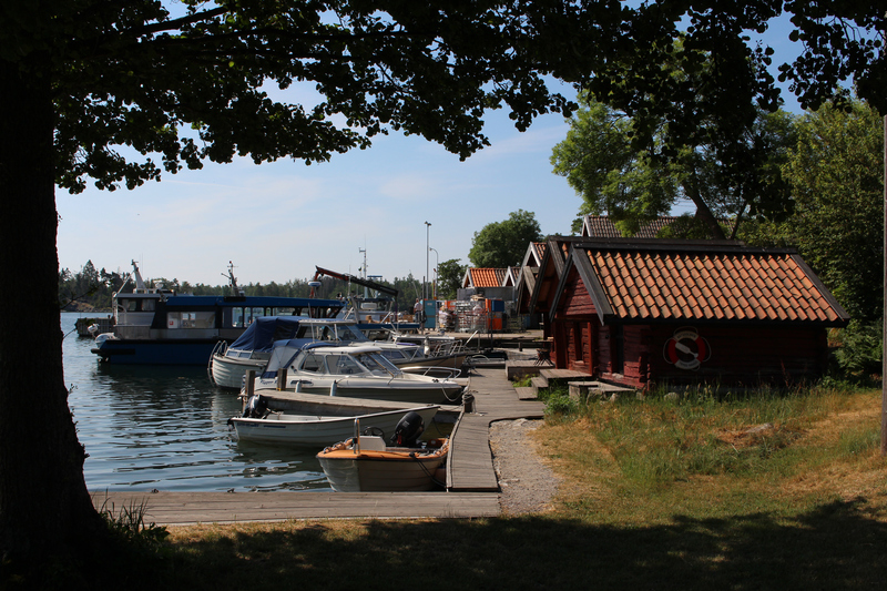 Båtar förtöjda i en småbåtshamn vid fiskebodar.