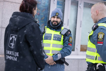 En kvinna med svart jacka med Norrtälje kommunlogga pratar med två manliga ordningsvakter i uniform
