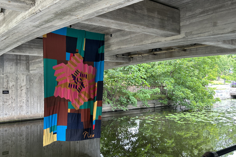 Ett konstverk i tyg hänger under en bro i Norrtäljeån