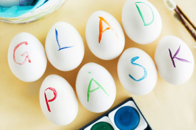 Åtta stycken vita ägg med en bokstav skriven på varje ägg. Bokstäverna bildar ordet Glad påsk. 