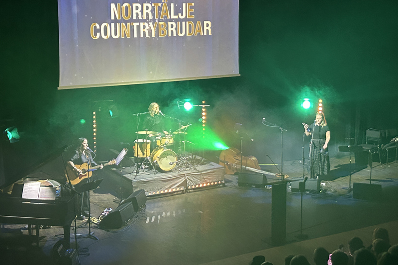 Tre kvinnor p&aring; scen som sjunger och spelar