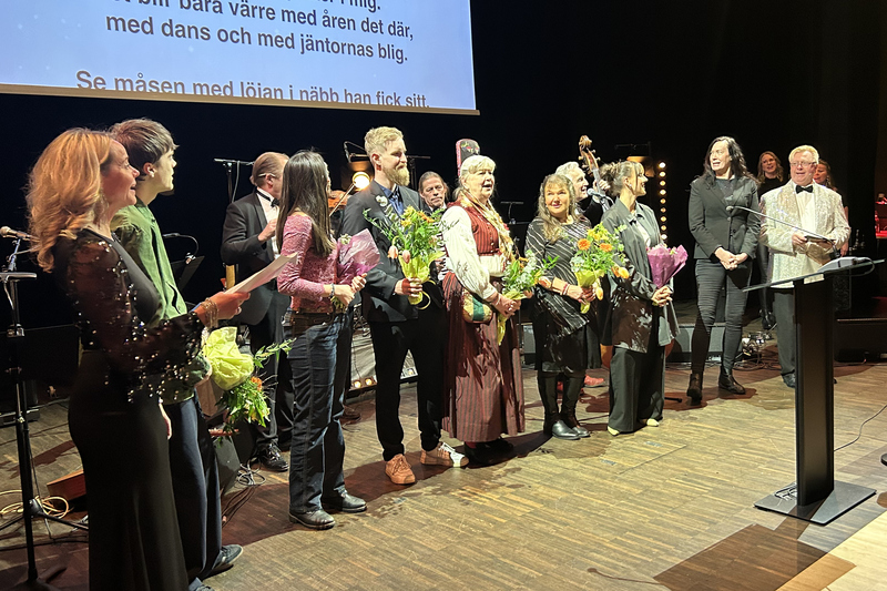Massa personer p&aring; en scen som sjunger. N&aring;gra h&aring;ller i en blombukett