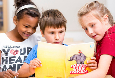 Tre barn läser en bok tillsammans.