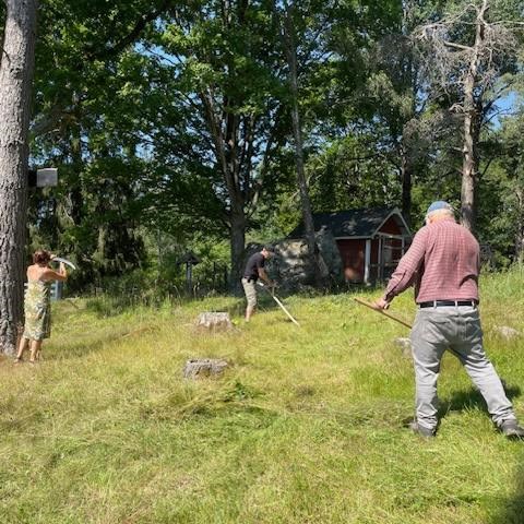 tre personer med lie som slår en äng