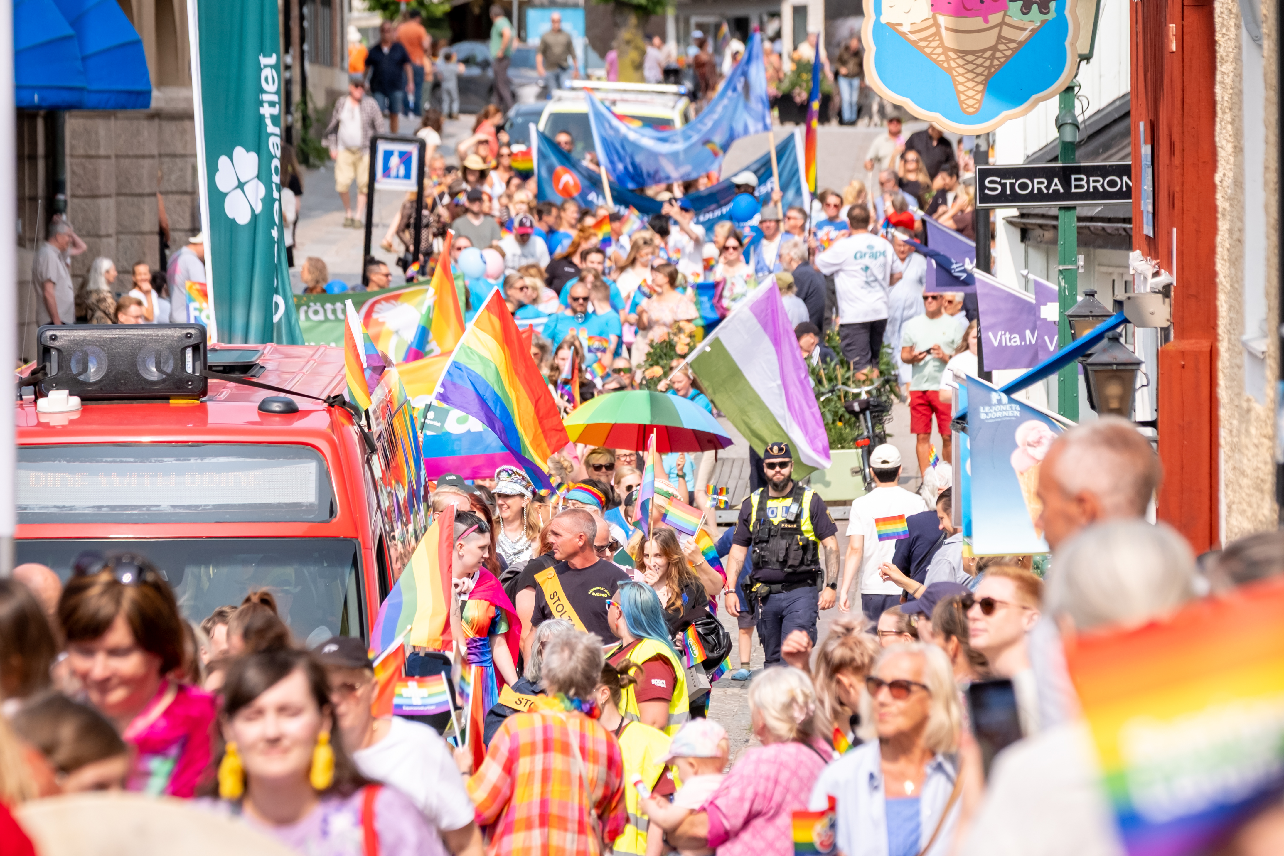 Bild från Roslagen Prides parad 2025 när ett färgglatt folkhav passerade Stora bron. I folkhavet syns prideflaggor och banderoller. Vädret är fint och folk är sommarklädda. 