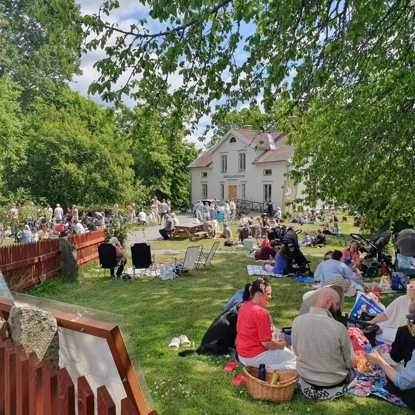 Bilden visar midsommarfirande på Färsna gård med besökare som har picknik på filtar i gräset