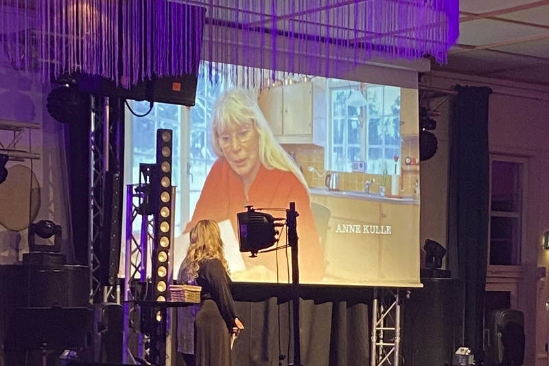 Skådespelerskan Anne Kulle visas på en stor skärm på scenen.