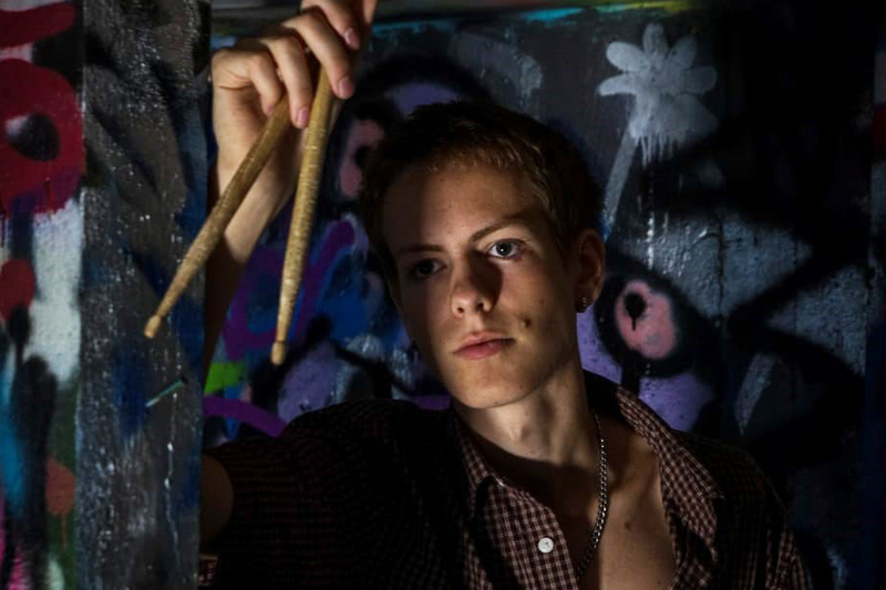 Ung man håller i trumpinnar. Graffiti i bakgrunden.