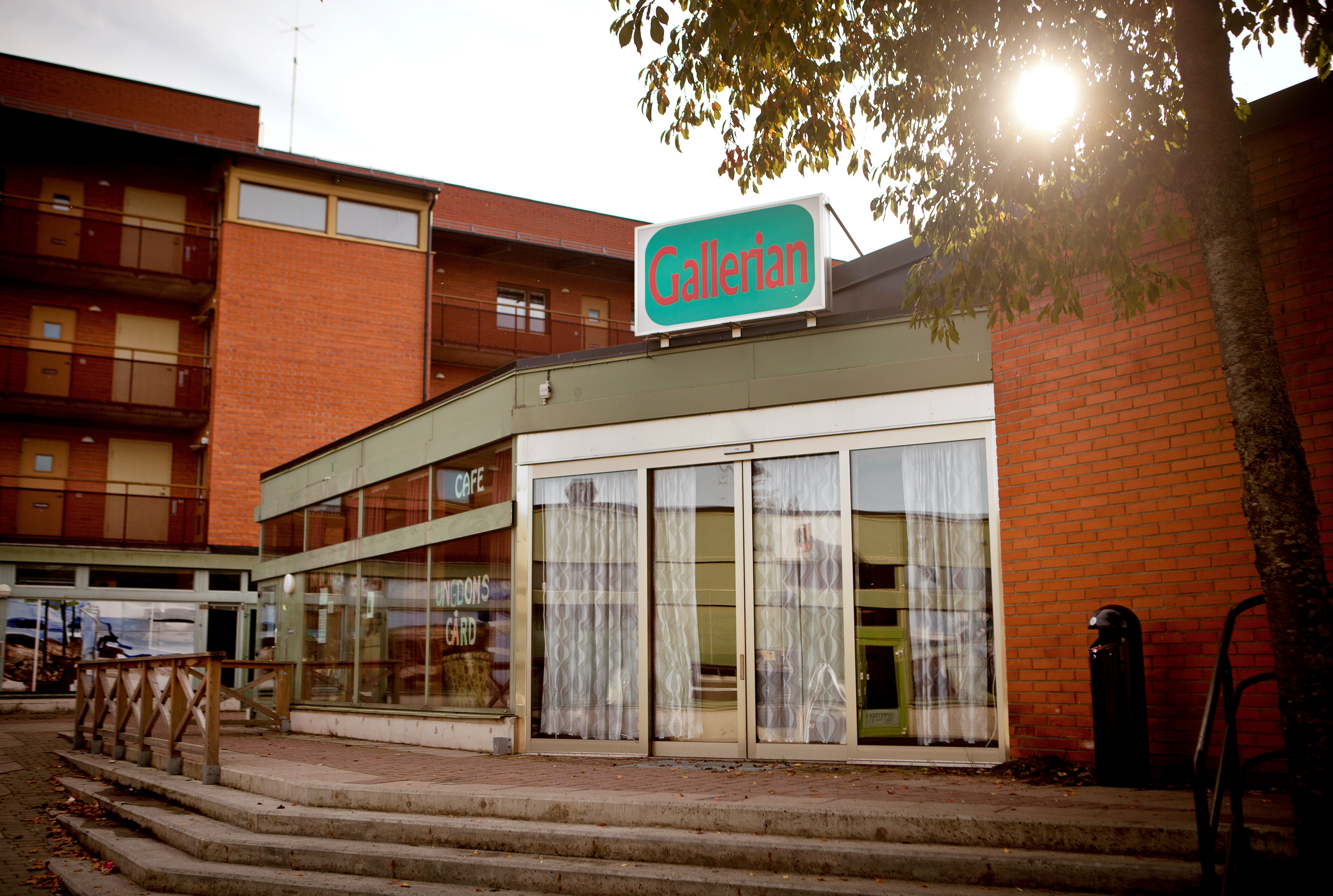 Tegelbyggnad med stora glasfönster. På taket sitter en turkos skylt där det står Gallerian