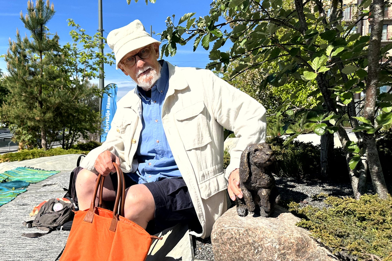 En man med hatt och en orange väska klappar en kanin i brons