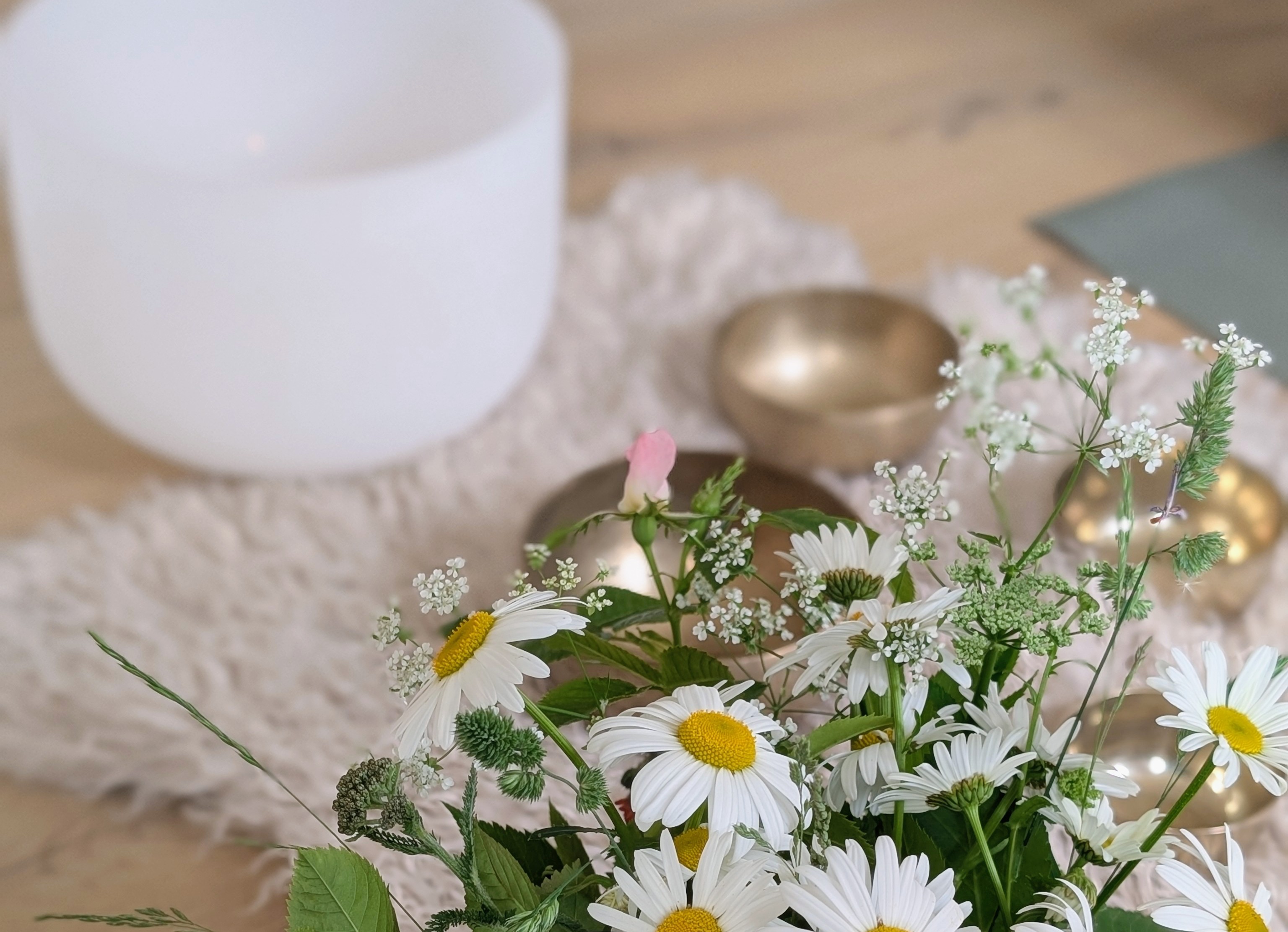 En närbild på klangskålar. Runtom dem ligger utspridda sommarblommor. 