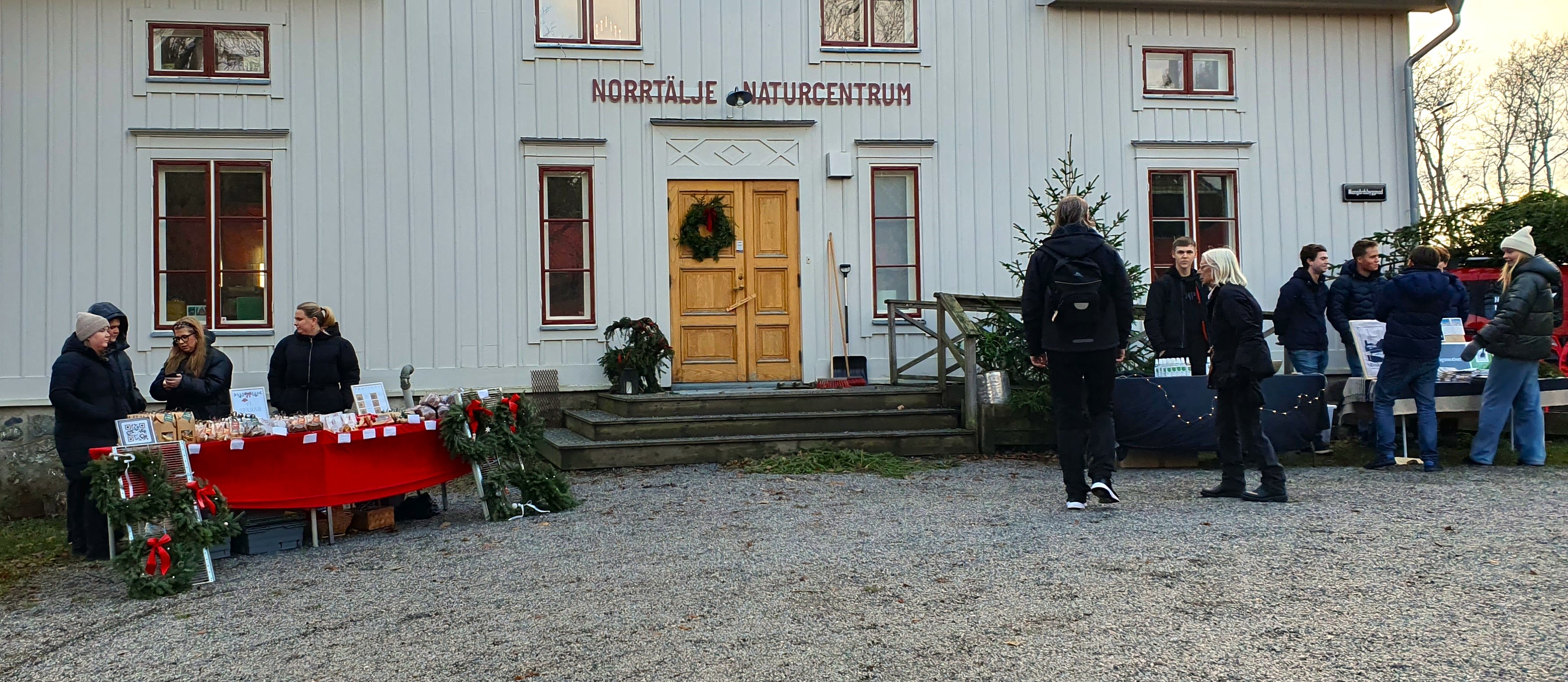Bilden visar marknadsstånd och besökare framför Mangårdsbyggnaden på Färsna gård, ett stort vitt hus med mycket folk i rörelse och julstämning i stånden