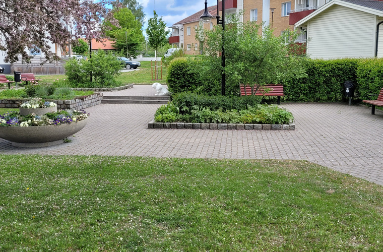 Bilden visar Bankparken i Hallstavik. På bilden ser man planteringar med perenner och parkbänkar där man kan vila sig i skuggan av ett träd.