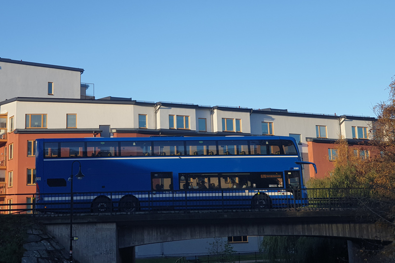 Blå buss som kör över en bro och byggnader i bakgrunden