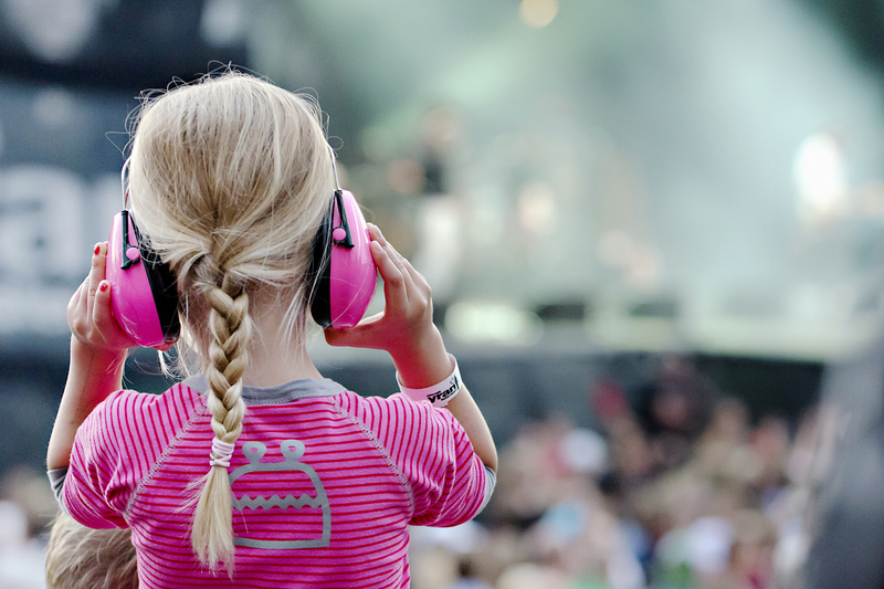 Barn som tittar på konsert med rosa hörselkåpor på sig.